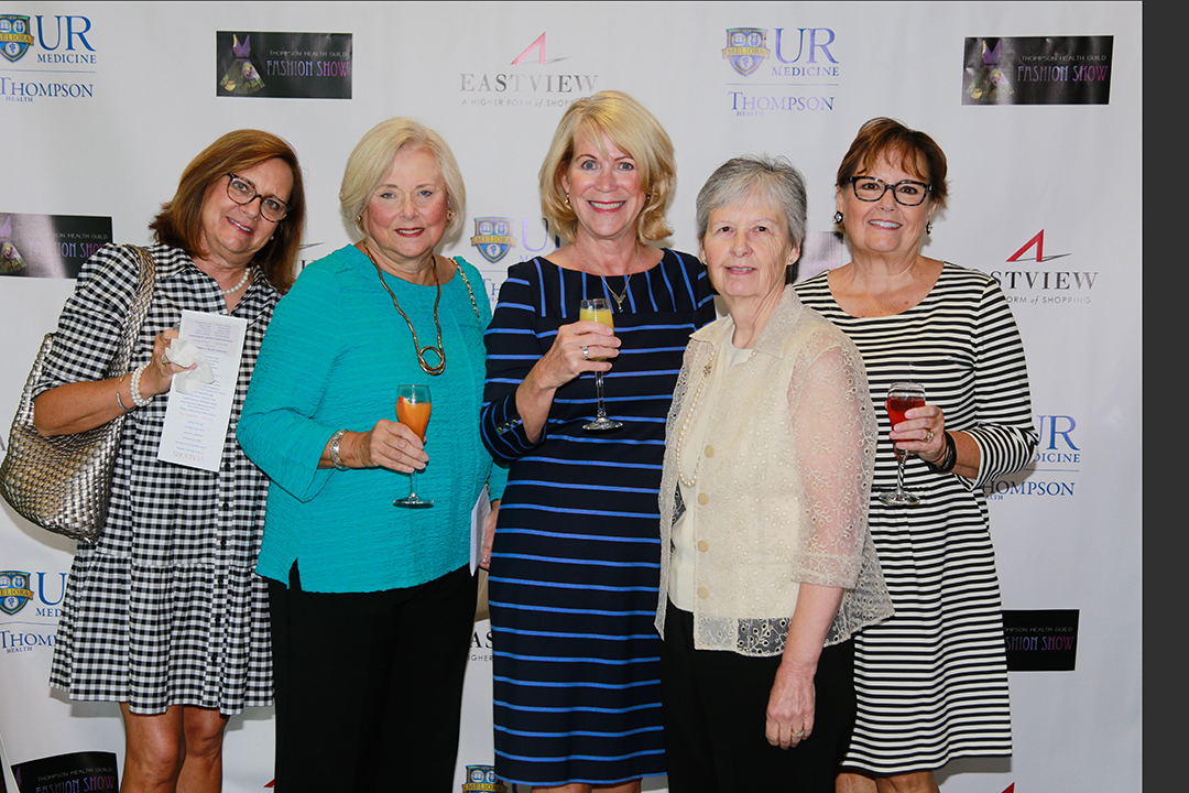 Photo of five elegant women at the fashion show in front of a backdrop holding glasses of champagne